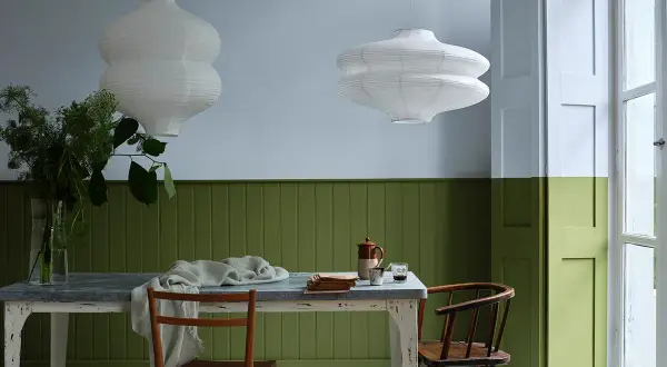 Tavola apparecchiata con sedie in legno, lampade bianche e pareti bicolore: un esempio di eleganti verde oliva abbinamenti.