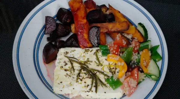 En tallrik med ugnsbakade rödbetor, sötpotatisstavar och en stor bit fetaost i ugn, toppad med örter. Serveras med en fräsch sallad.