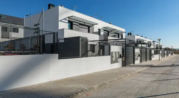 Modernos chalets adosados blancos con vallas metálicas y puertas de garaje.