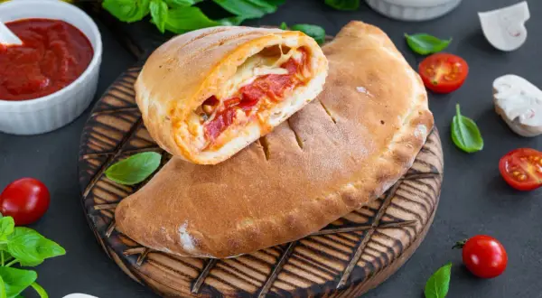 Pyszny calzone przepis: złociste ciasto z sosem pomidorowym i serem, podane z pomidorkami i bazylią.