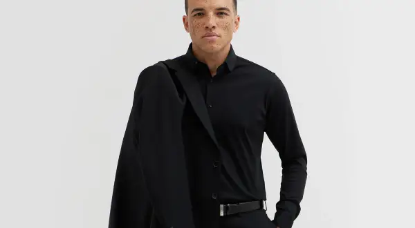 Mężczyzna w czarnym garniturze, z marynarką na ramieniu. Elegancki, czarny pasek do garnituru podkreśla jego styl.