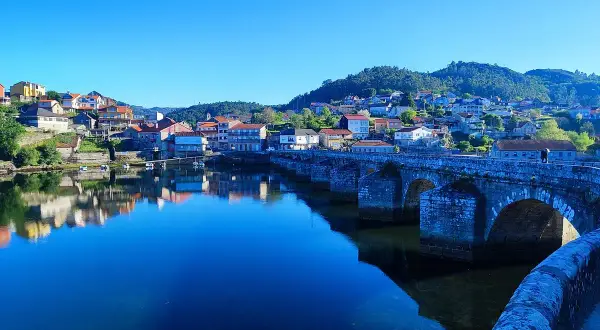 Puente de piedra en Ponte Sampaio, con casas reflejándose en el río azul bajo un cielo despejado.