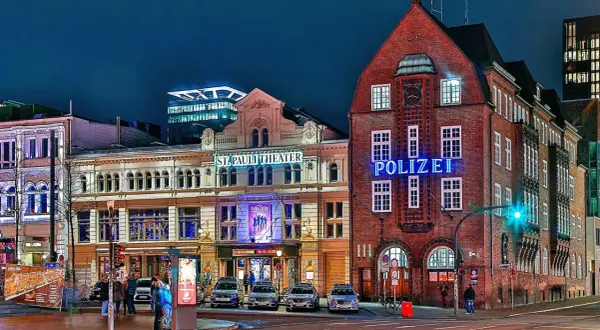 Polizeigebäude und St. Pauli Theater in Hamburg bei Nacht, mit leuchtenden Schildern und Autos.