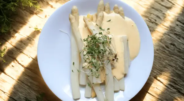 En tallrik med vit sparris, täckt av en krämig sås och toppad med färska groddar. En härlig vårmåltid.