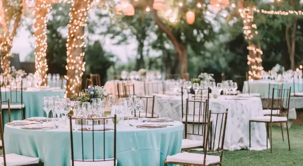 Tables dressées pour un mariage jardin féerique, éclairées par des guirlandes lumineuses dans les arbres.