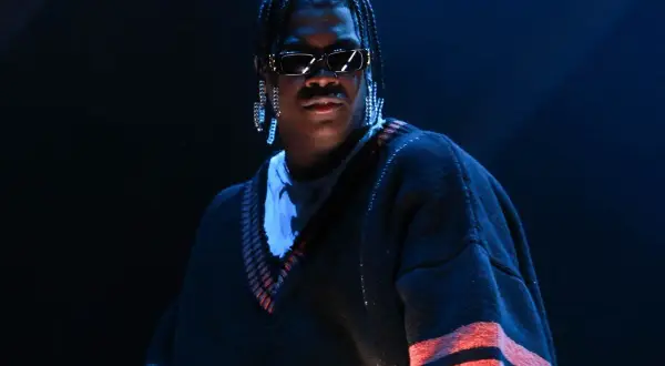 Lil Yachty w Polsce, w okularach i z długimi kolczykami, w swetrze z czerwonymi pasami.