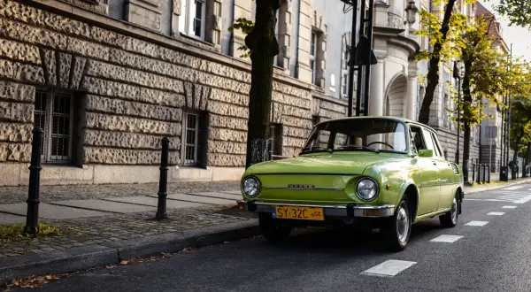 Zielona Skoda 105/120 na tle zabytkowej kamienicy. Ile lat musi mieć budynek żeby był zabytkiem? Ten ma ponad 100 lat.