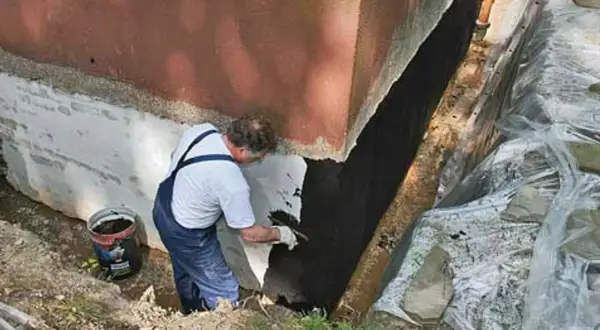 Mann trägt Bitumenanstrich innen auf die Kellerwand auf.