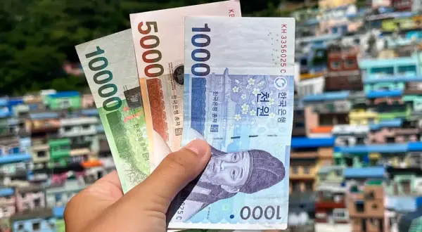 Dłoń trzyma banknoty wonów, pokazując korea południowa ceny. W tle kolorowe domy na wzgórzu.