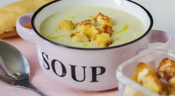 Kremowa zupa z selera naciowego z grzankami w różowej miseczce z napisem "SOUP".