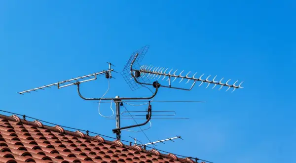 Na dachu domu, pod błękitnym niebem, zamontowana jest wieloelementowa antena TV.