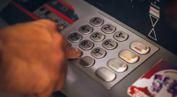 Dłoń wpisuje PIN na klawiaturze bankomatu, symbolizując dostęp do usług finansowych i **open banking**.
