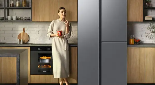 Elegancka kobieta z truskawkami obok nowoczesnej lodówki dwudrzwiowej z kostkarką.