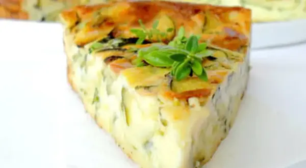 Tranche de clafoutis courgettes dorée et moelleuse, garnie de quelques feuilles de basilic frais.