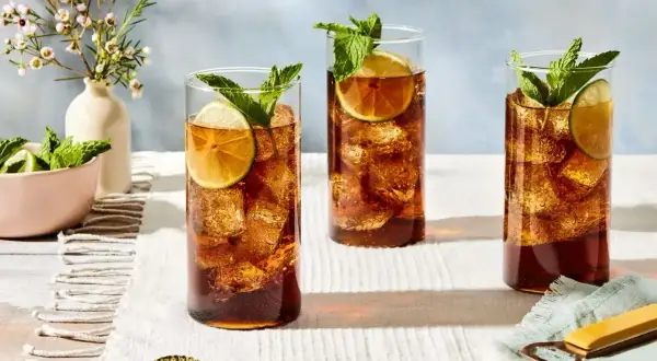 Trzy szklanki orzeźwiającego whisky z colą, ozdobione plasterkami limonki i listkami mięty, stoją na białym obrusie.