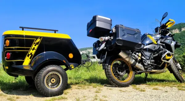 Une remorque pour chien moto, noire et jaune, est attelée à une moto BMW tout-terrain, prête pour une aventure en plein air.