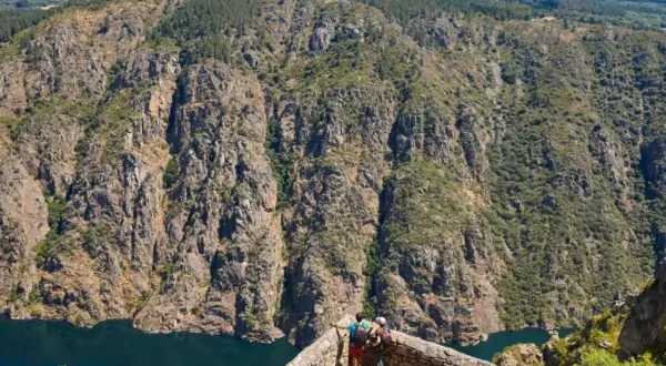 Dos excursionistas contemplan la majestuosidad de los ríos de Galicia, serpenteando entre cañones rocosos y bosques frondosos.