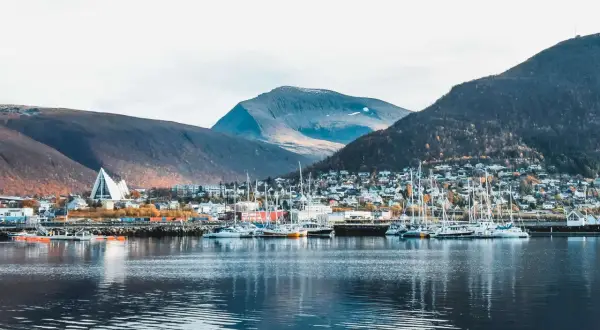 Tromsø im Sommer: Segelboote im Hafen vor einer Stadt am Berghang, gekrönt von der markanten Eismeerkathedrale.
