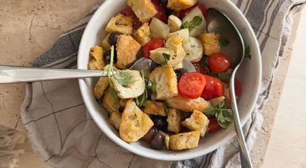Herzhafter Brotsalat mit Roggenbrot, Kirschtomaten, Oliven und Artischockenherzen, garniert mit frischen Kräutern.