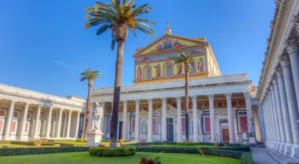 Giardino curato davanti alla Basilica San Paolo, con palme alte e statue.