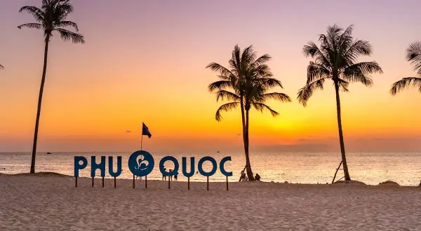 Zachód słońca na plaży Phu Quoc, Wietnam. Palmy i napis "PHU QUOC" na tle pomarańczowego nieba.