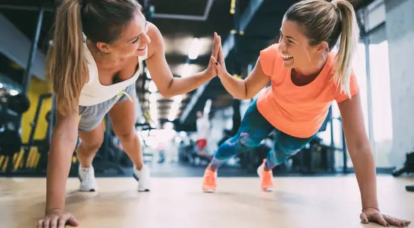 Dwie uśmiechnięte kobiety robią pompki w siłowni, świętując sukces. Chcesz wiedzieć, jak zdobyć kartę Multisport?