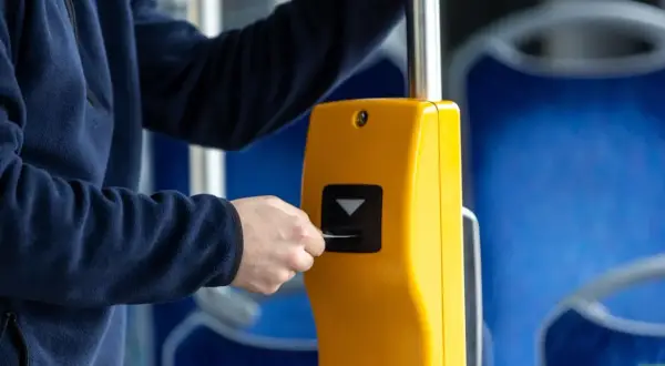 Osoba wkłada kartę do żółtego kasownika w autobusie, pokazując, jak kupić bilet.