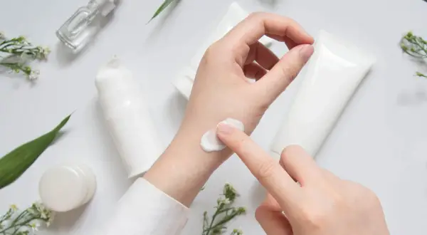 Eine Hand testet eine weiße Creme, umgeben von Pflegeprodukten und zarten Blüten. CI 45410.