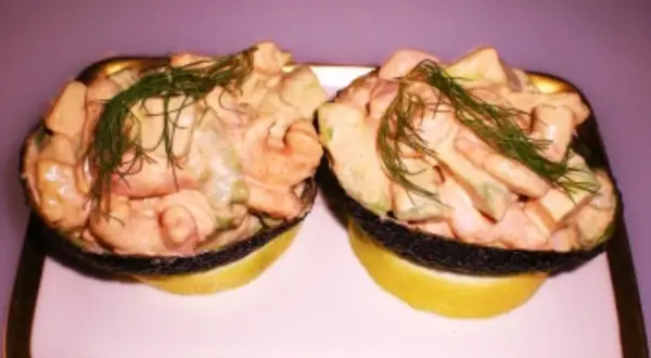 Zwei Avocadohälften gefüllt mit einem cremigen Krabbencocktail mit Avocado und Dill garniert, serviert auf Zitronenscheiben.