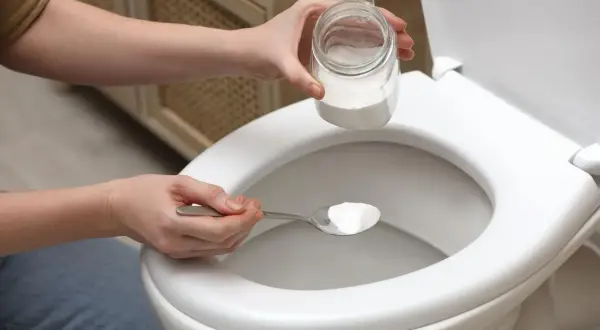 Une personne utilise une cuillère de bicarbonate de soude comme déboucheur canalisation maison pour un WC.