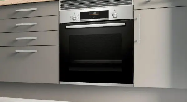 Moderno horno integrado en una cocina con cajones grises y encimera de madera.