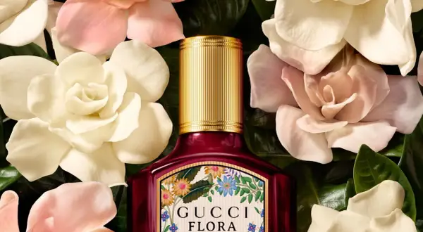 Perfumy Gucci by Gucci Flora w otoczeniu delikatnych kwiatów. Złota nakrętka i bogata etykieta z motywem roślinnym.