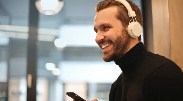 Uśmiechnięty mężczyzna w słuchawkach bezprzewodowych trzyma telefon, pokazując, jak podłączyć słuchawki bezprzewodowe do telefonu.