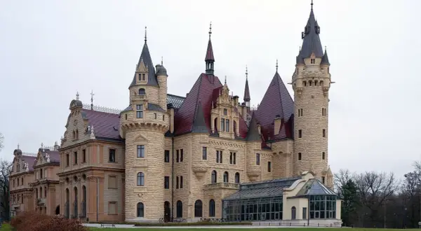 Imponujące pałace w Polsce, z wieżami i czerwonymi dachami, otoczone zielenią.