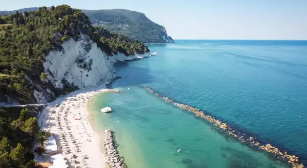 Spiaggia di Marina Palmense con scogliere bianche, mare azzurro e ombrelloni colorati.