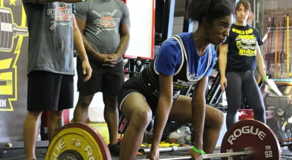 Atleta si prepara per uno stacco da terra, concentrata. Un evento di powerlifting e weightlifting con pubblico e attrezzature.