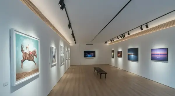 Galeria sztuki z nowoczesnym oświetleniem obrazów. Widać dzieła z jeźdźcem na koniu i krajobrazy.