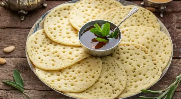 Une assiette de crêpes mille trous dorées, garnie d'une coupelle de miel et de menthe fraîche. Parfait pour un petit-déjeuner gourmand.