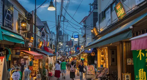 En livlig gata i gamla Tokyo med butiker, skyltar och människor som promenerar.