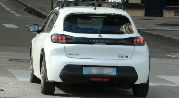 Voiture blanche avec équipement de **voiture radar embarqué** sur le toit, circulant dans une rue de Lyon.