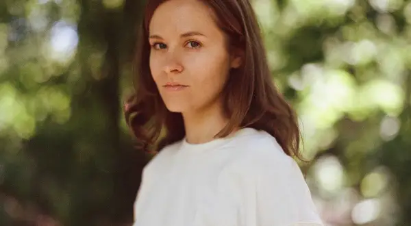 Hania Rani Esja, artystka o hipnotyzującym spojrzeniu, w białej bluzie na tle zieleni.