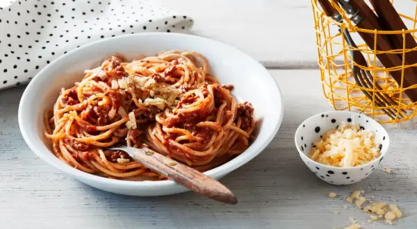Ein Teller Spaghetti Bolognese, ein Klassiker unter den spaghetti rezepte, mit geriebenem Käse bestreut. Daneben eine Schale mit extra Käse.
