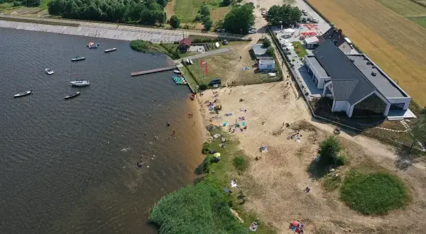 Słoneczny dzień nad zalewem Cedzyna. Ludzie odpoczywają na plaży, pływają i żeglują.
