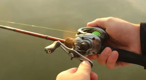 Dłonie trzymają wędkę z kołowrotkiem, gotowe do rzutu. Precyzyjne **casting spinning** to klucz do sukcesu.