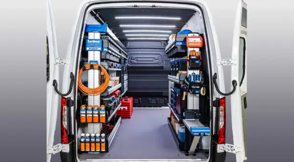 Interior de un autobús camperizado en España, organizado con estanterías y herramientas.