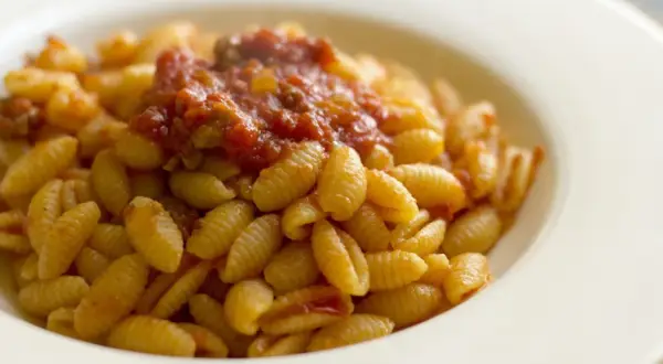 Malloreddus alla campidanese, pasta sarda con sugo di pomodoro e salsiccia, serviti in un piatto bianco.
