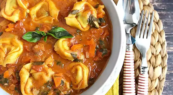 Miseczka tortellini w sosie pomidorowym z bazylią, obok sztućców.