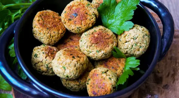 Köstliche Falafel, frisch zubereitet nach einem einfachen falafel rezept, liegen in einer schwarzen Schüssel, garniert mit Petersilie.