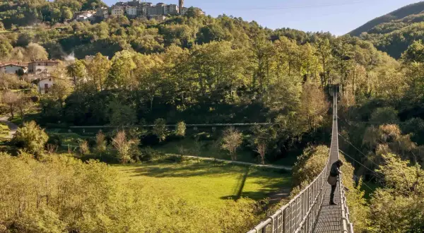 Una persona osserva il panorama dal ponte sospeso delle Ferriere, con un borgo arroccato sulla collina sullo sfondo.