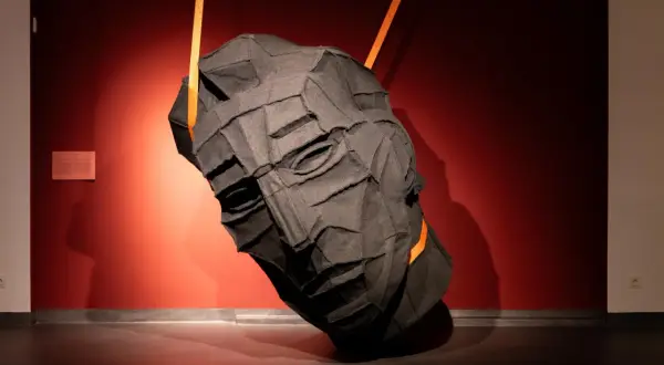 Mroczna, tekstylna głowa wisi na pomarańczowych pasach w muzeum sztuki współczesnej Gdańsk.